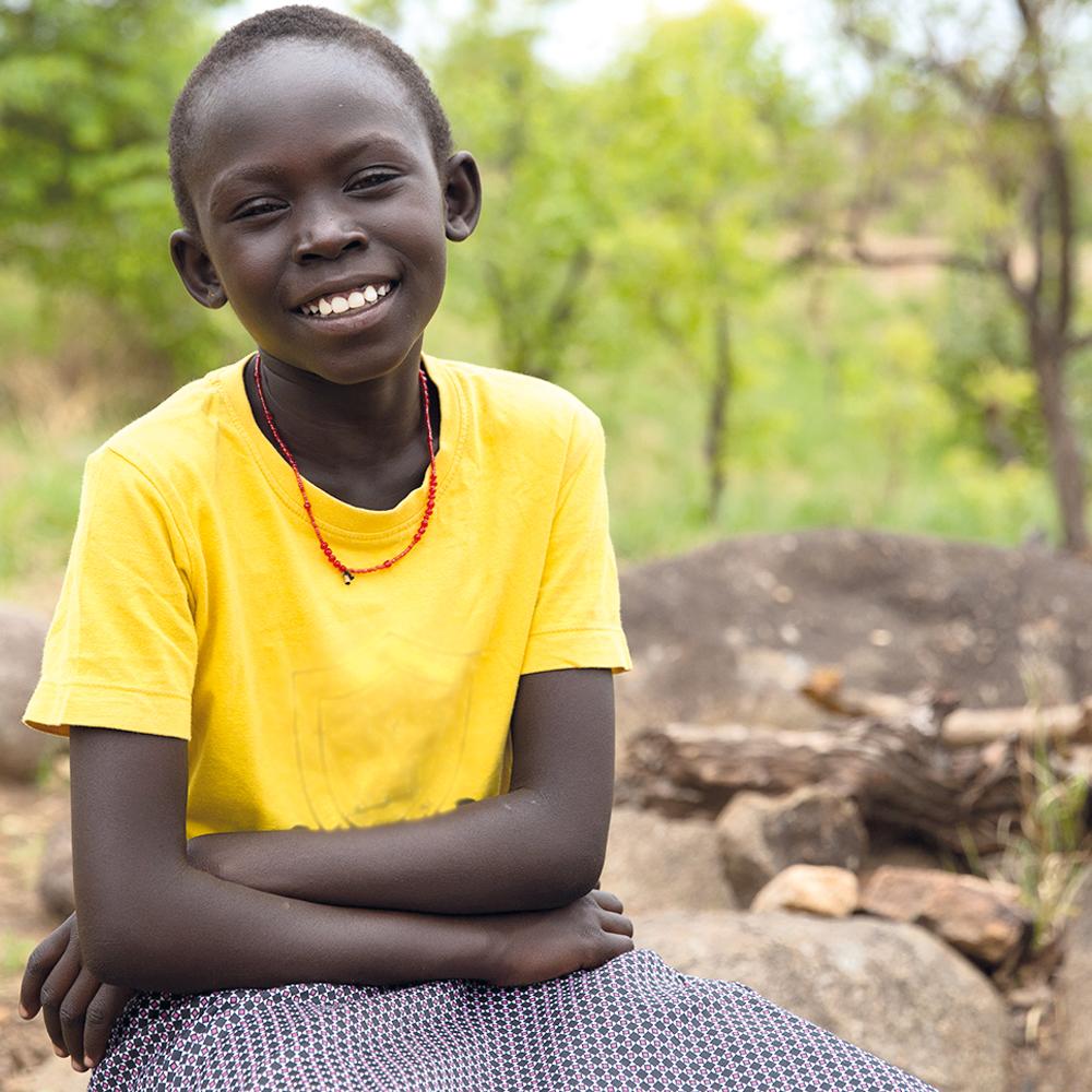 Doruka, now smiling in Uganda wearing a vibrant yellow t-shirt