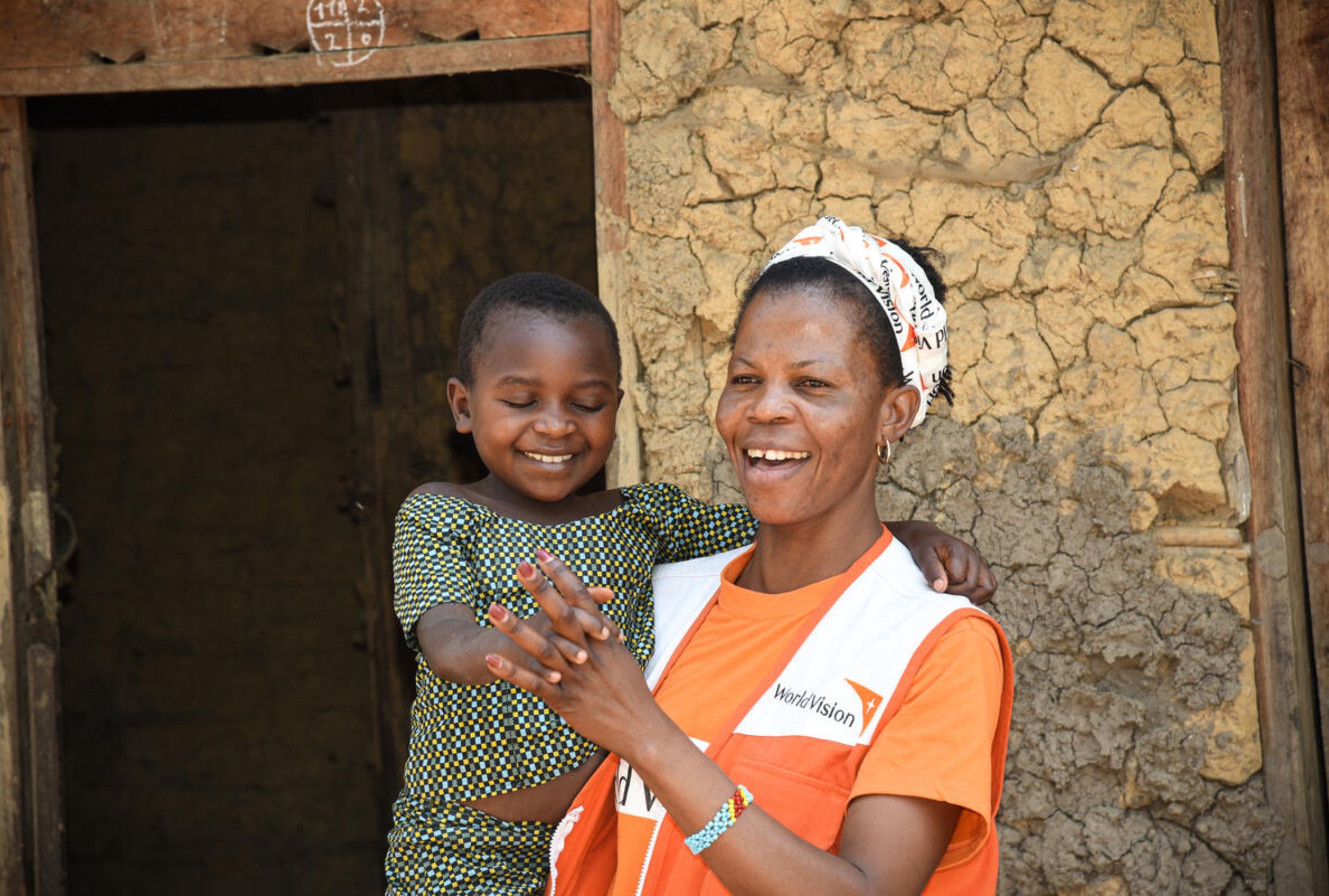 A member of the World Vision's team in DRC holding a young girl, both smiling
