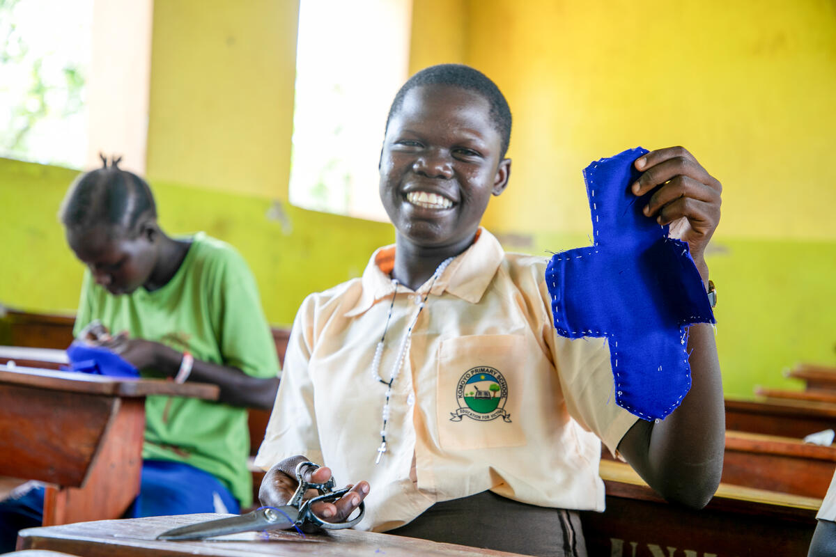 Teenage girl from Uganda holding up a sanitary pad she made in class, while smiling