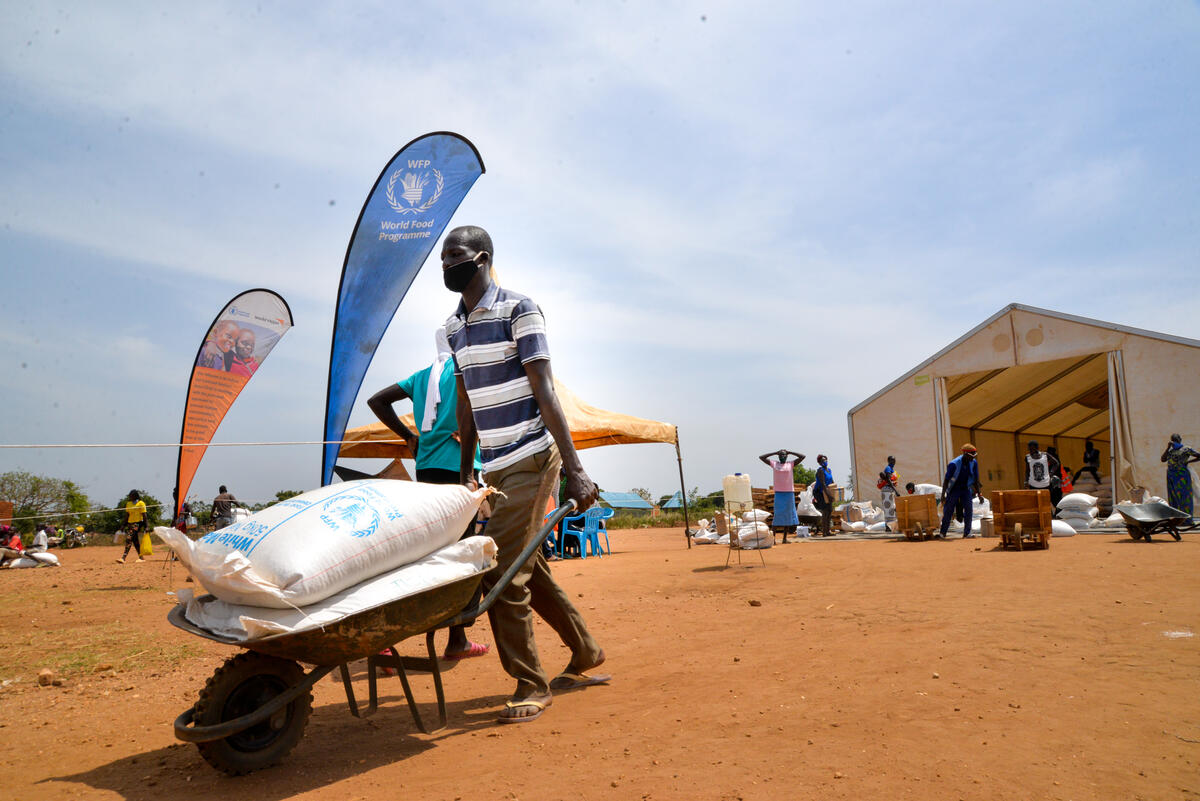 Ugandan man pushing a wheel barrow holding a large supply of food supplies from the World Food Programme and World Vision