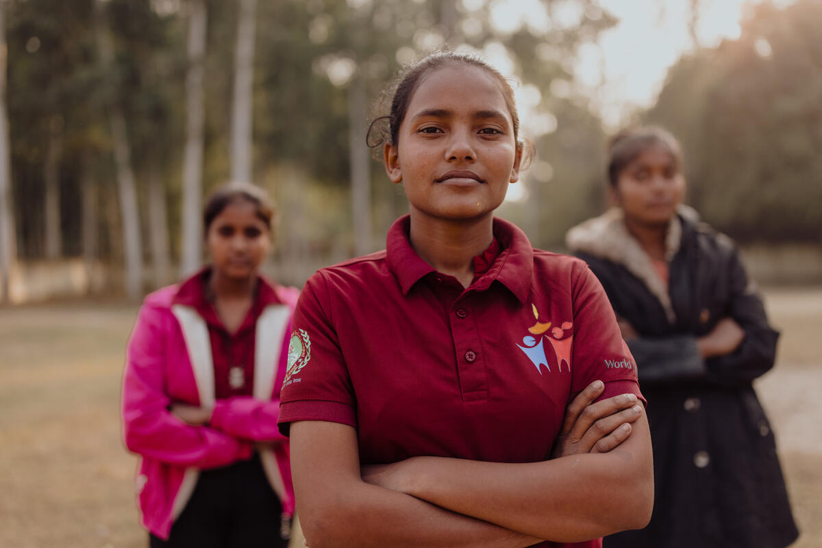 Three teenage girls from Nepal stand confidently, arms crossed, looking into the camera