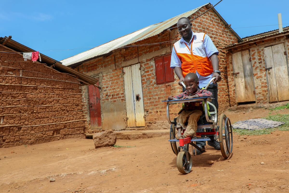 A World Vision staff member pushes a young child in a wheelchair