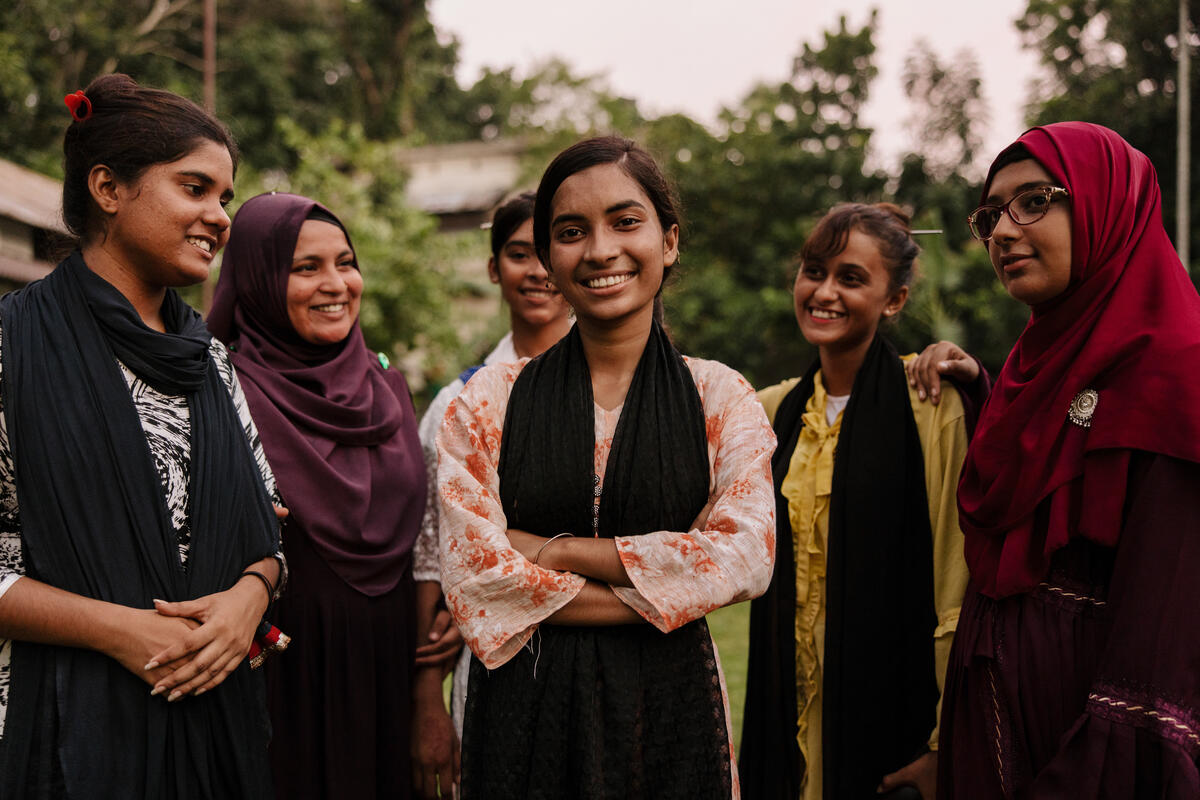 A group of teenage girls in Bangladesh stand together, smiling at the camera