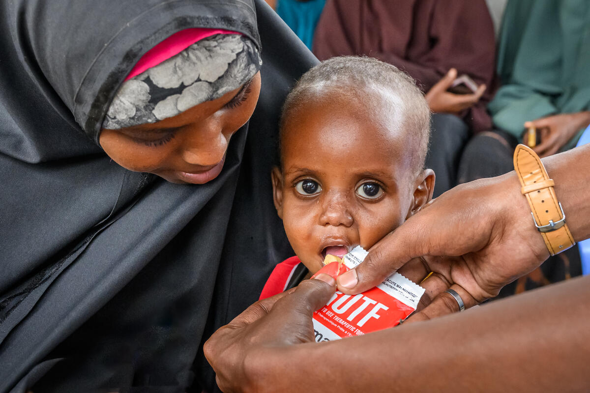 A child being fed from an orange packet with two hands