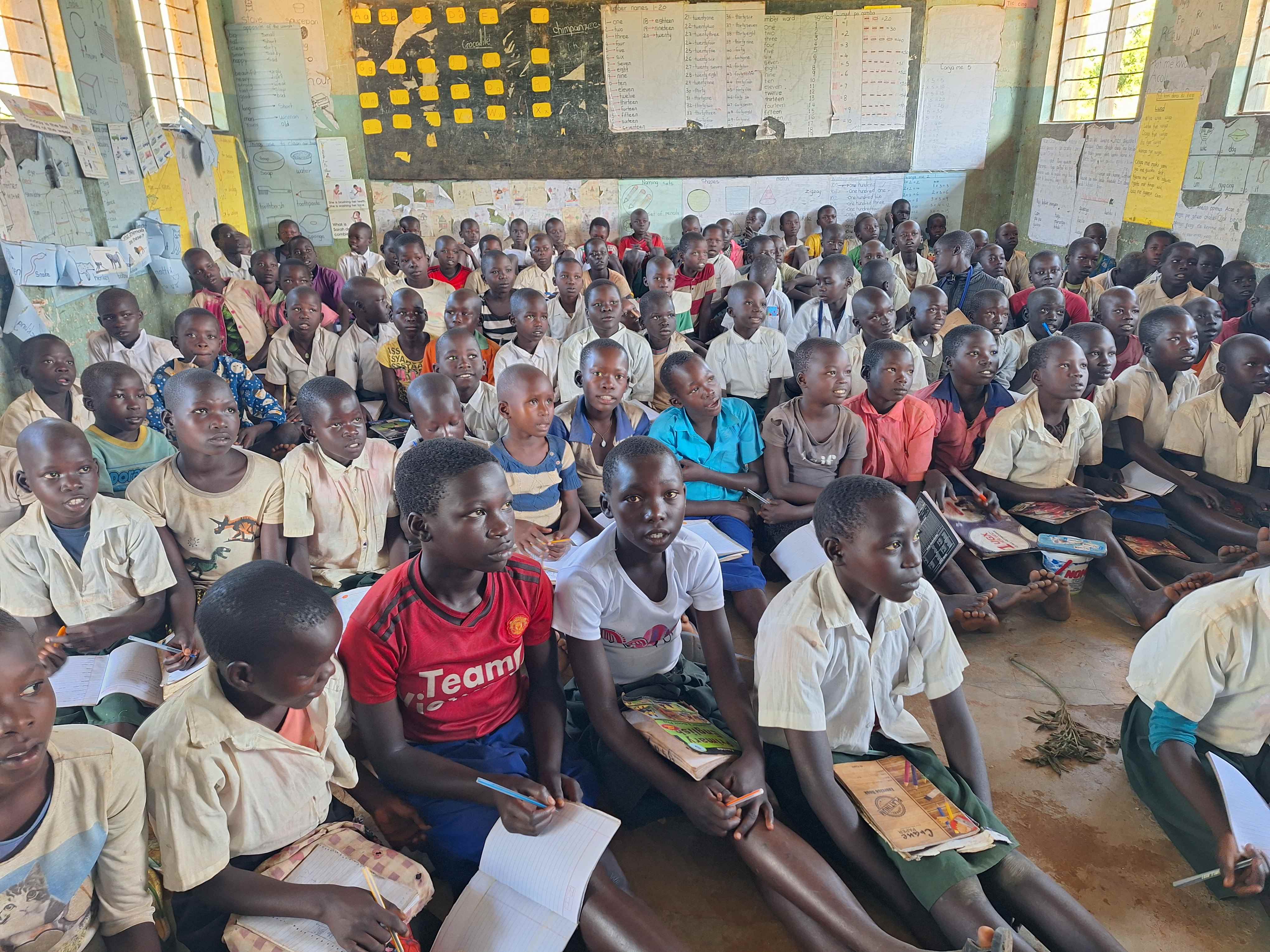 Children sat in overcrowded Ugandan school classroom, on the floor, without desks.