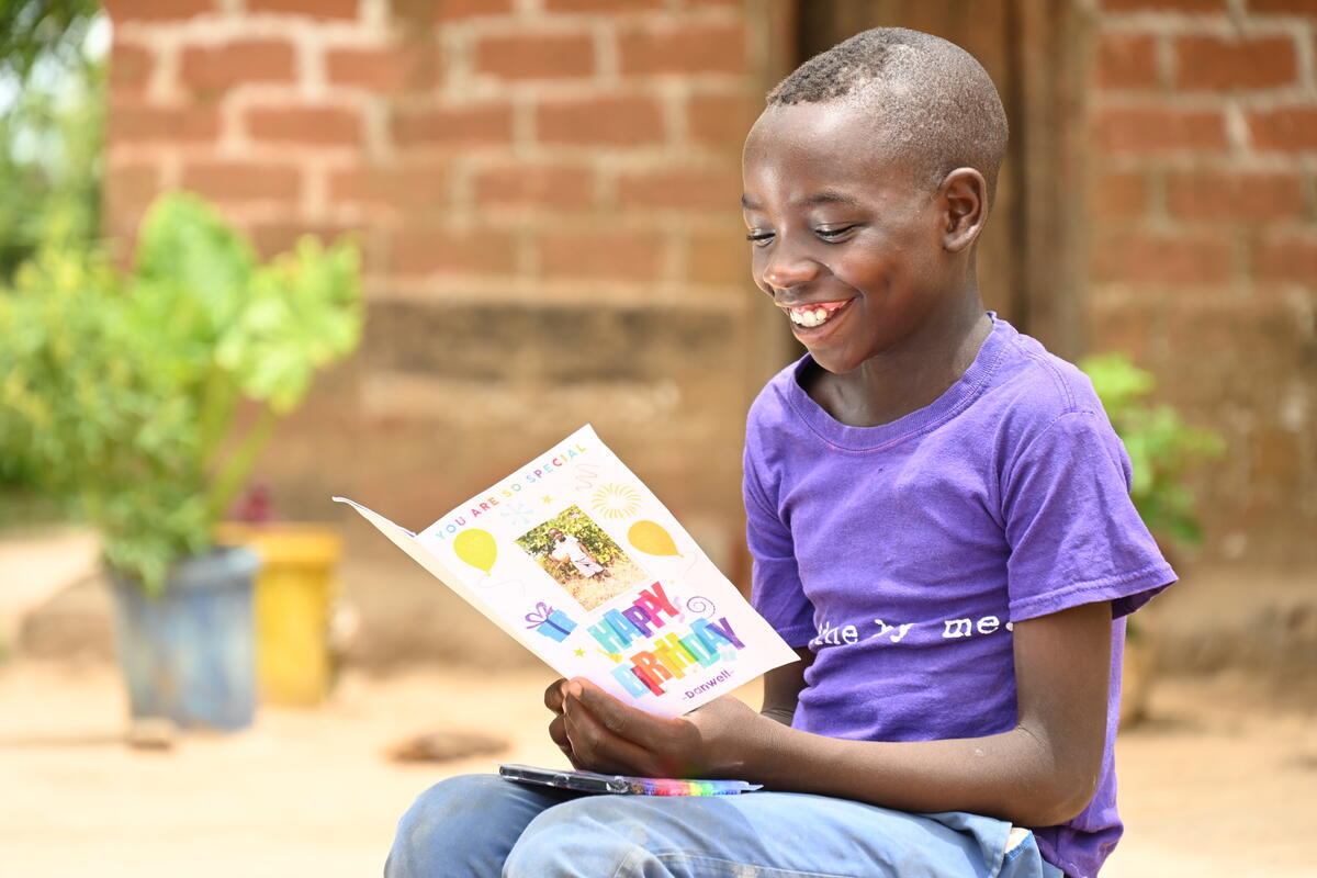 A child in Zambia smiles as they read a birthday card from their sponsor