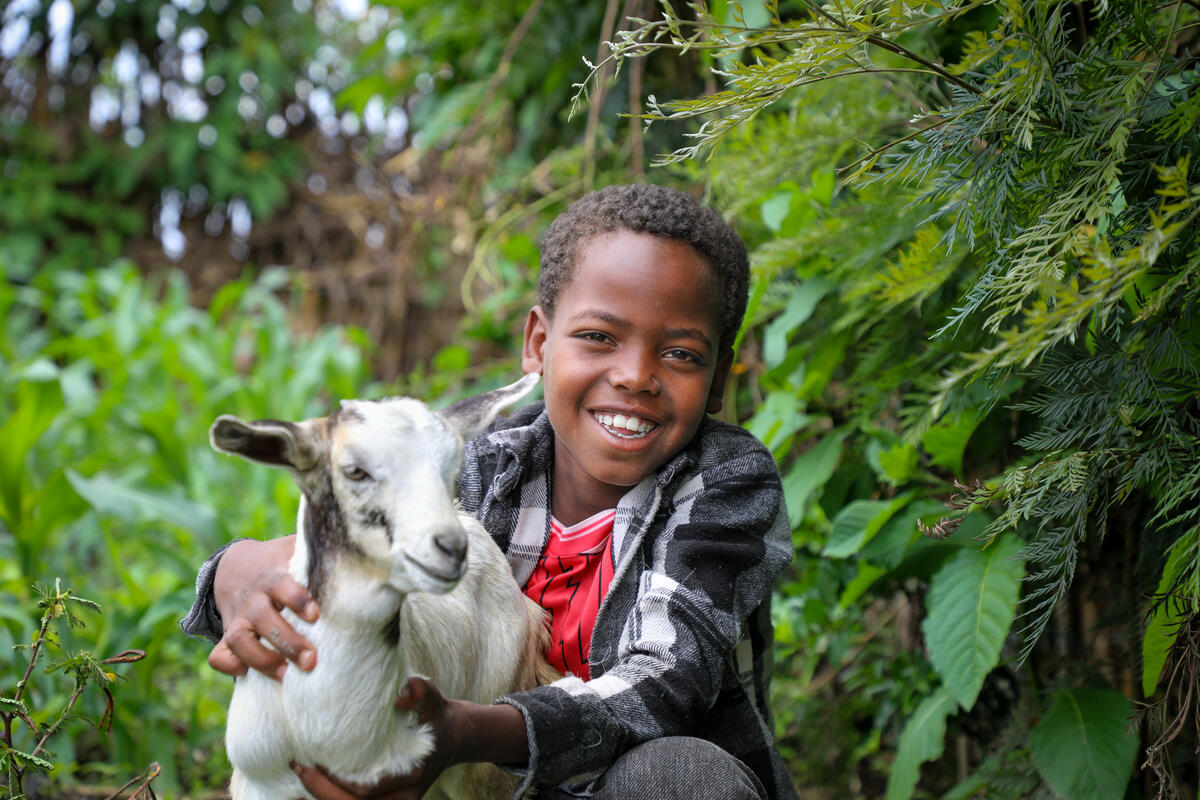 Child from Ethiopia standing outside holding a goat and smiling to the camera