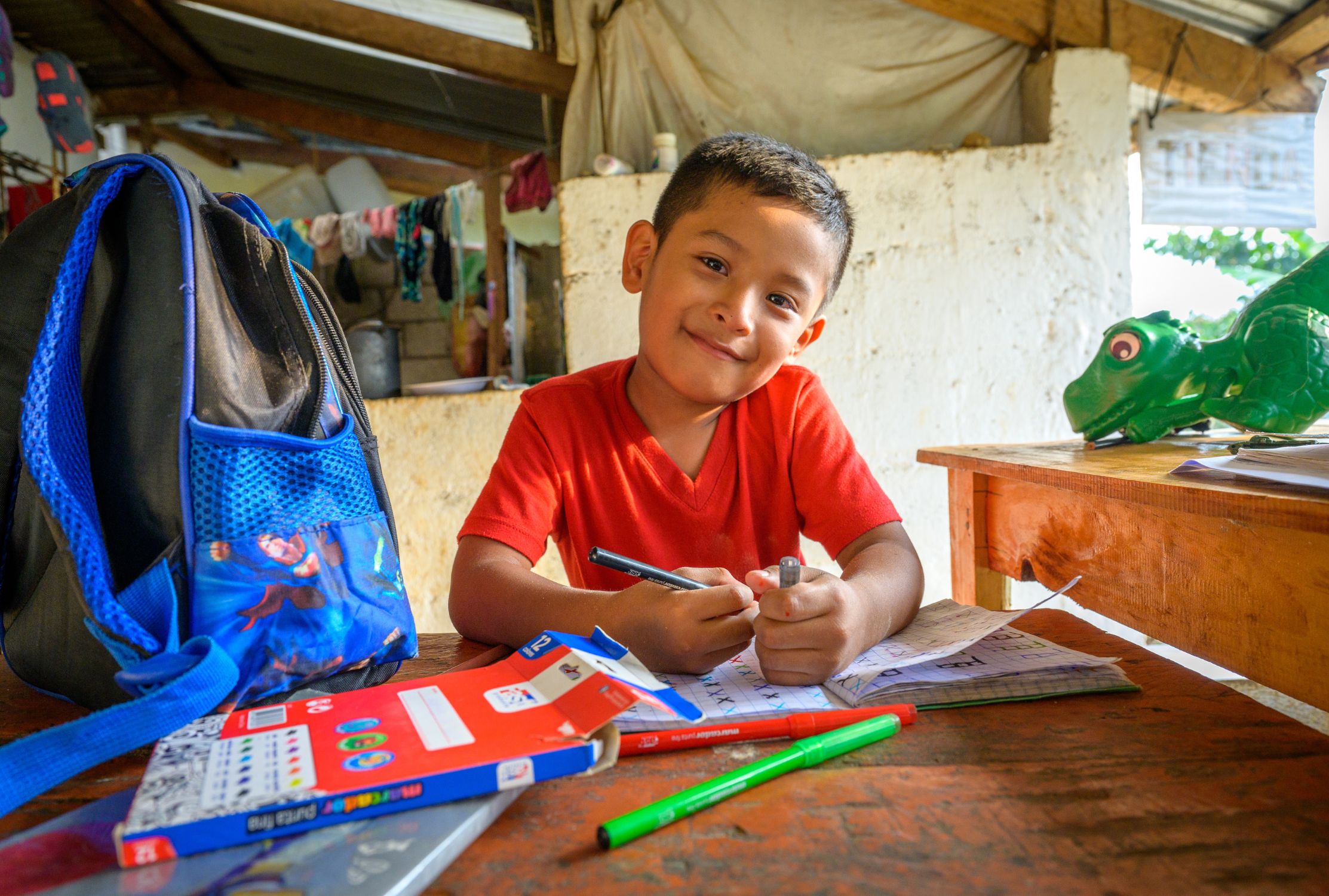 Boy from Guatemala sits at a desk and smiles with his school books