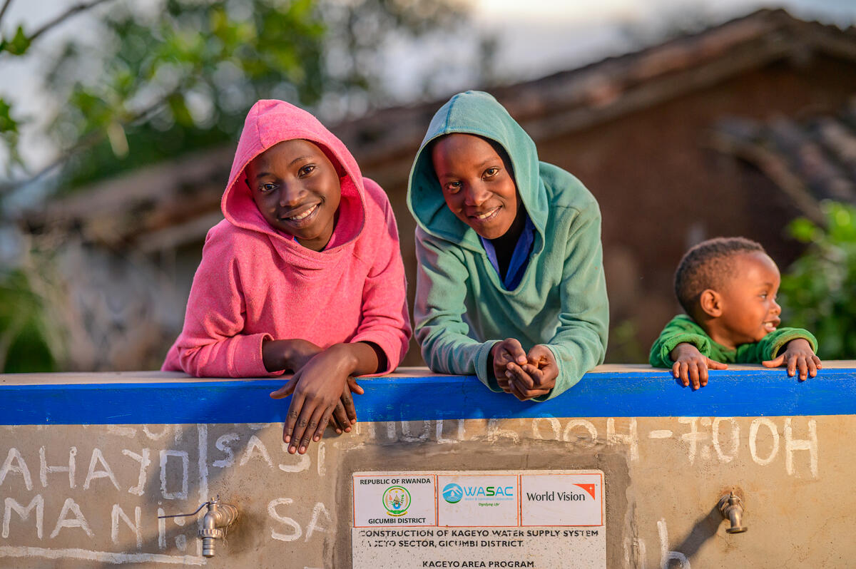 Two teenagers and a toddler pose by a newly installed water collection point