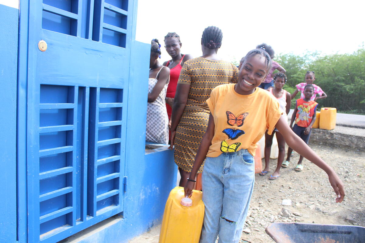 Haitian teenage girl carrying a water container and smiling