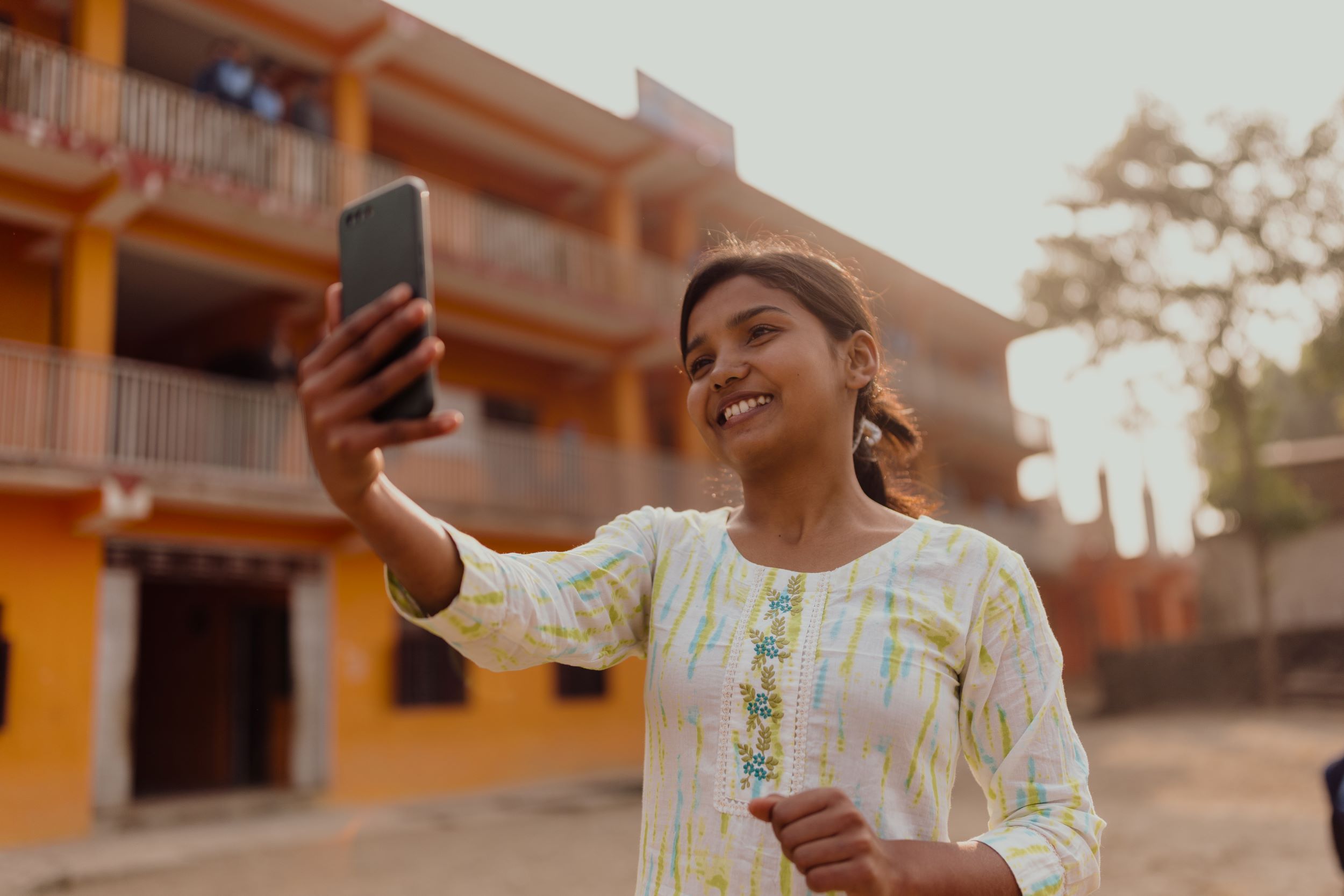 Nepali girl in cream dress taking selfie in front of bright yellow building 