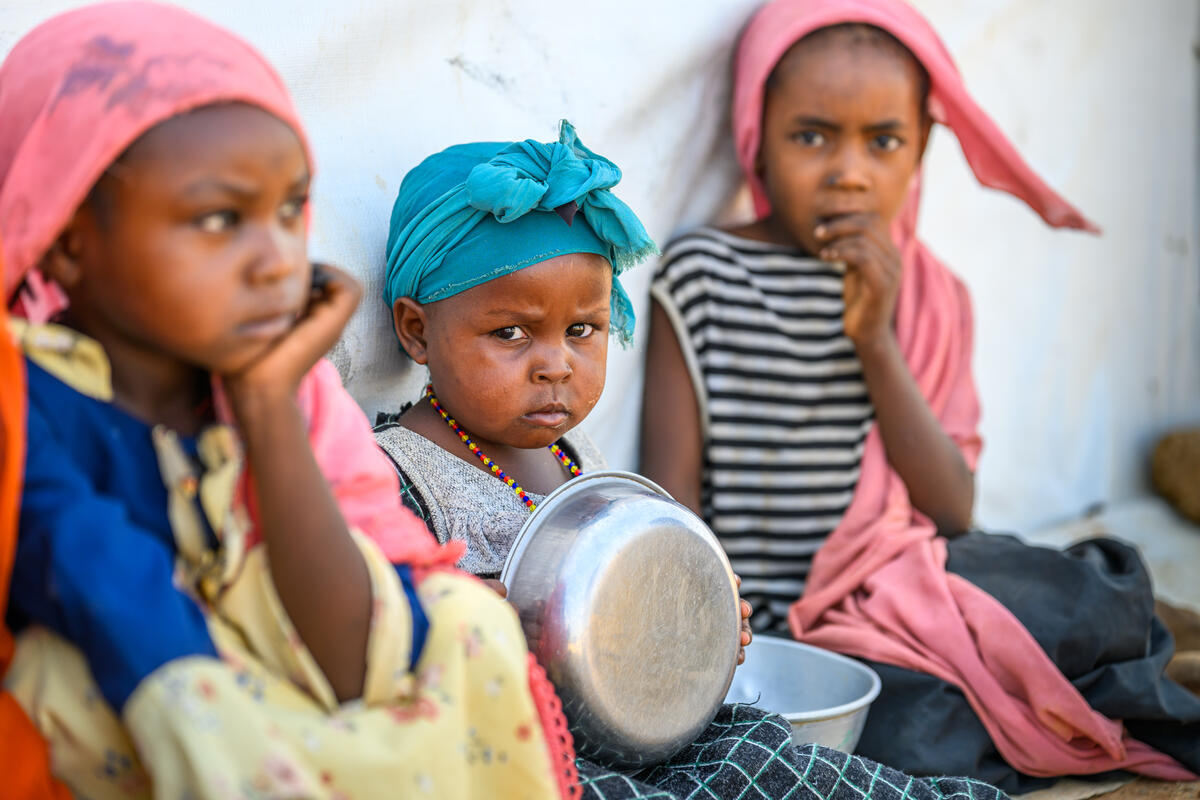 Three Sudanese refugee children holding empty bowls 