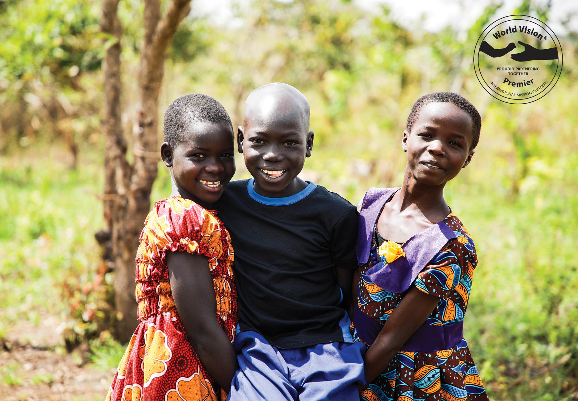 Three children in Uganda smile to camera.