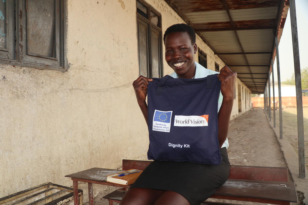 A girl from South Sudan holding a sanitary kit containing sanitary pads, underwear, water, and soap 