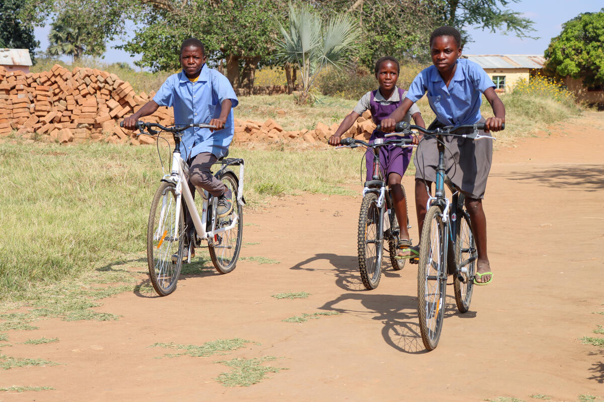 Girls in school uniform, smiling as they ride their bicycles 