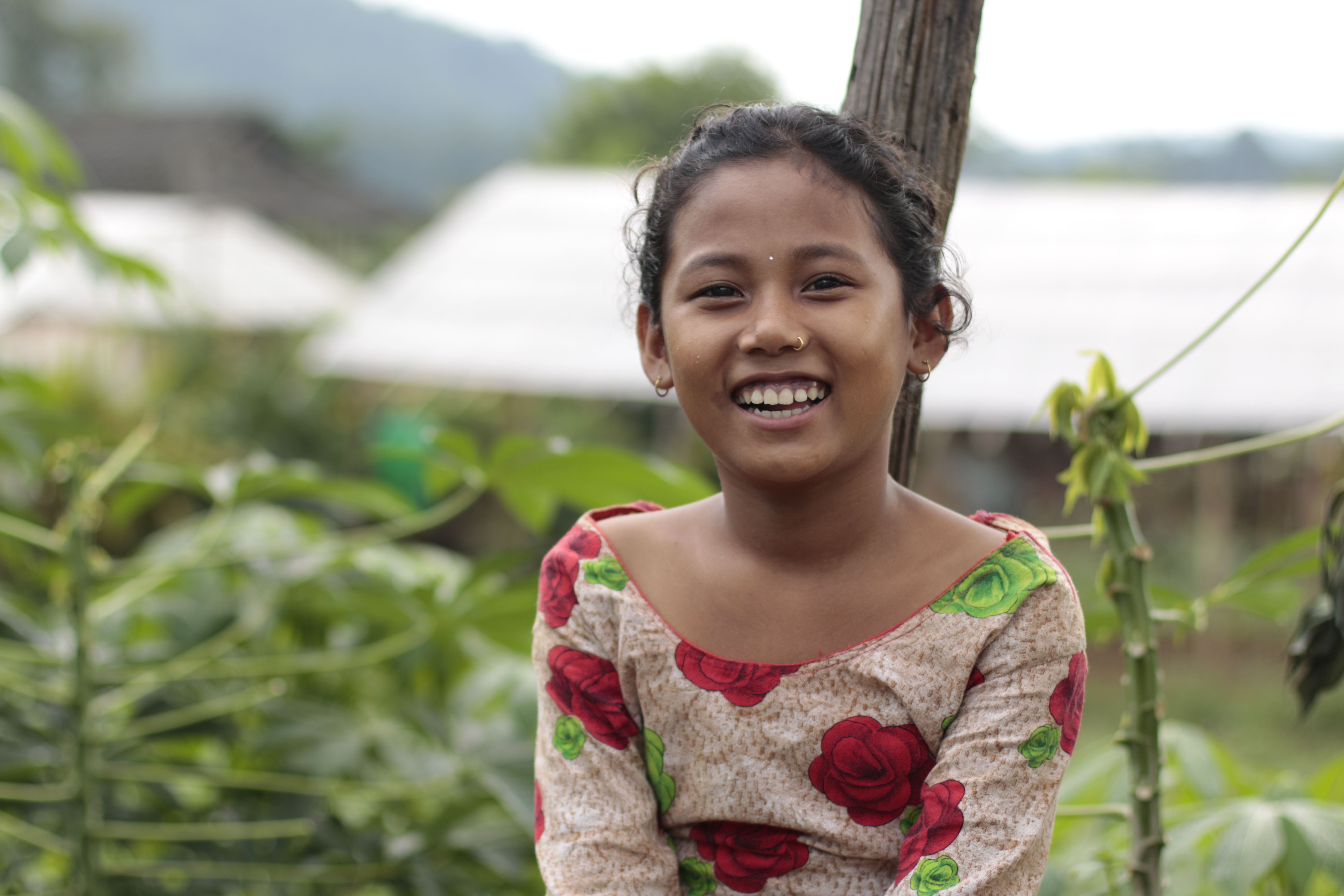 Sponsored child from Nepal smiles, sitting outside in front of foliage