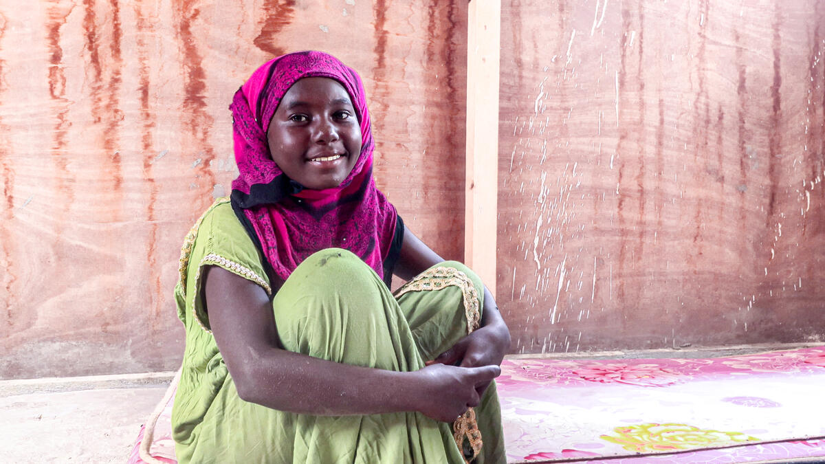 Yemeni refugee girl smiles and looks at the camera while sat in her tent