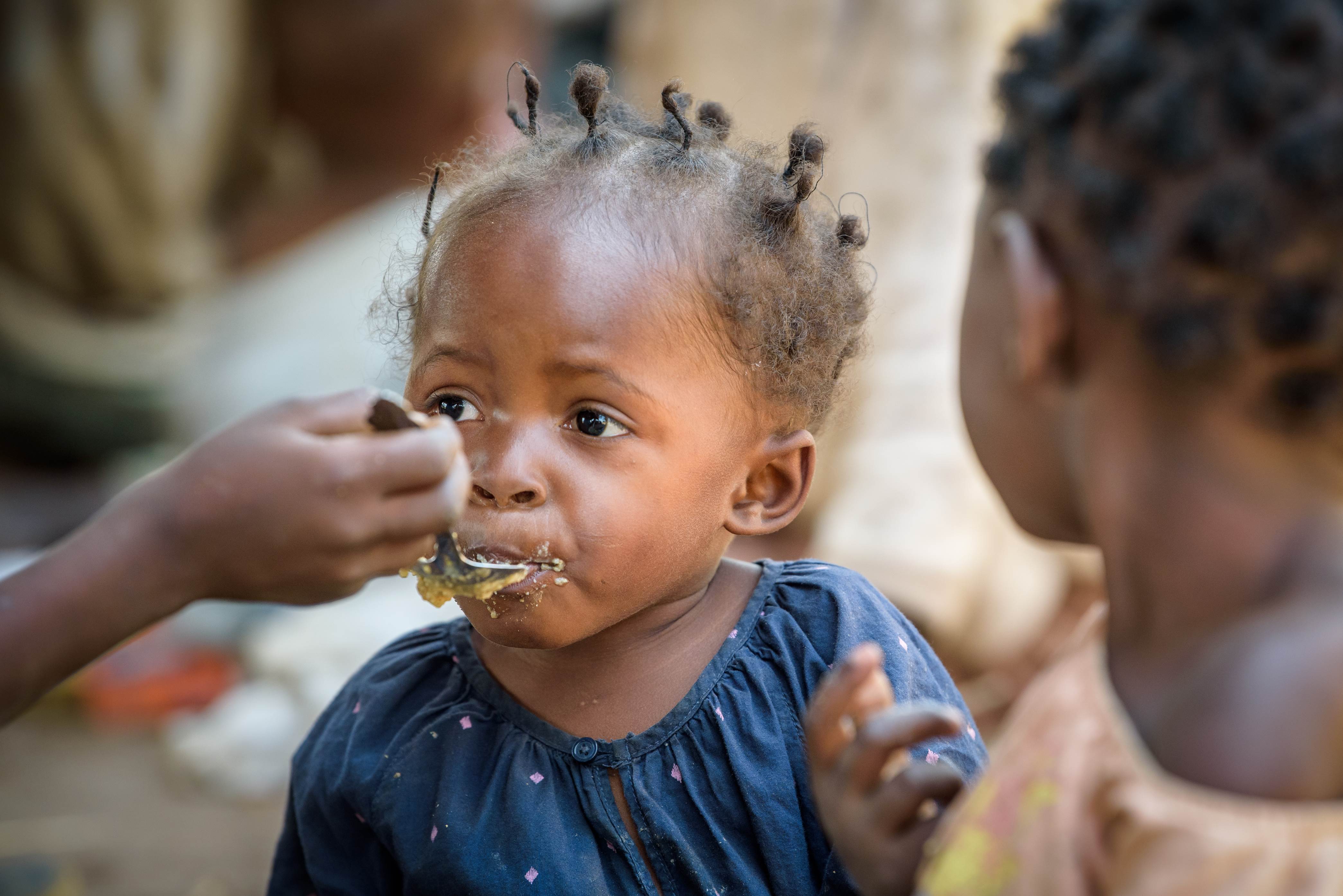 Young girl from the DRC being fed with a spoon by another child (not in frame)