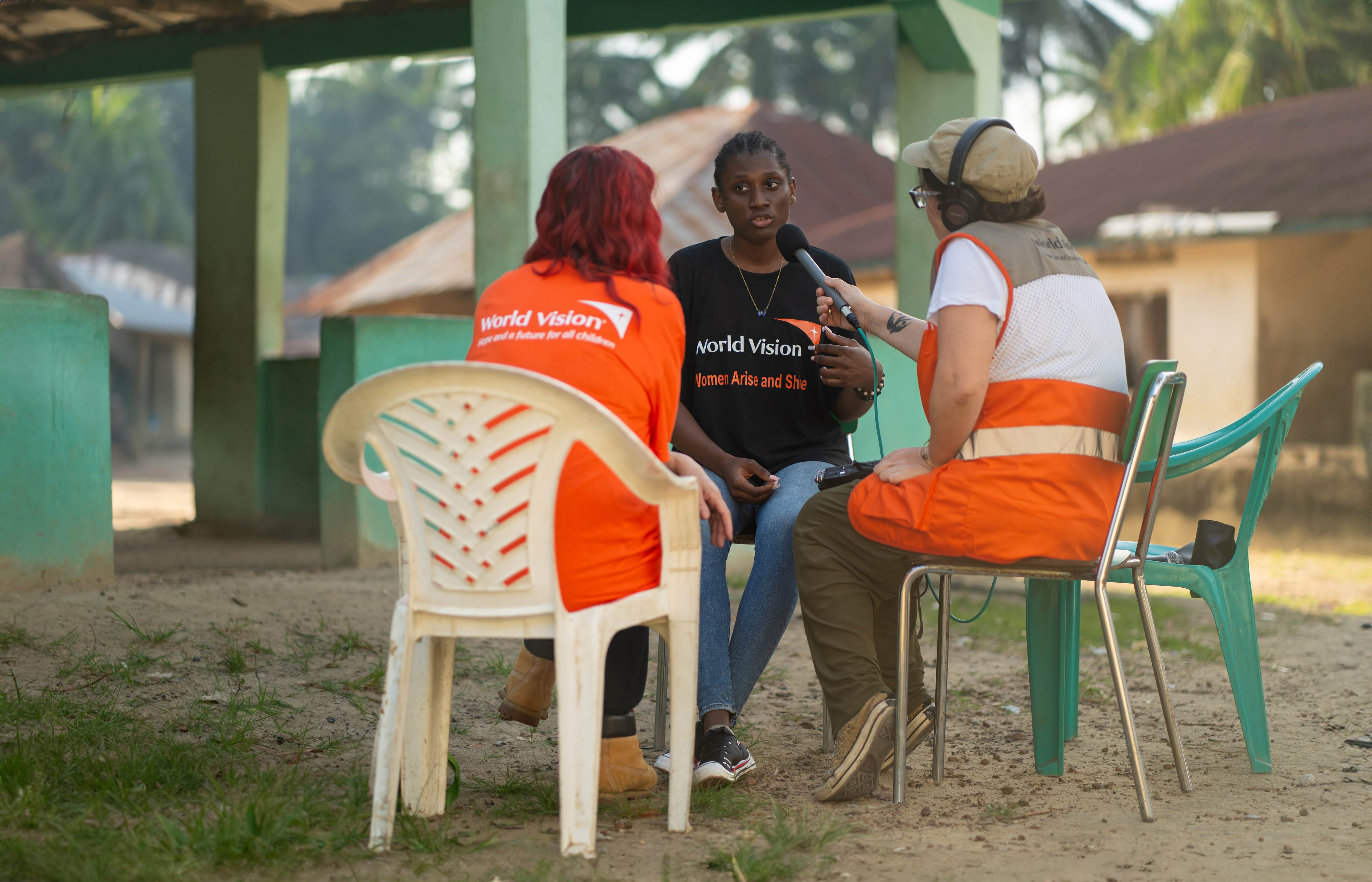 A broadcaster and sound person interview a young adult woman in Sierra Leone