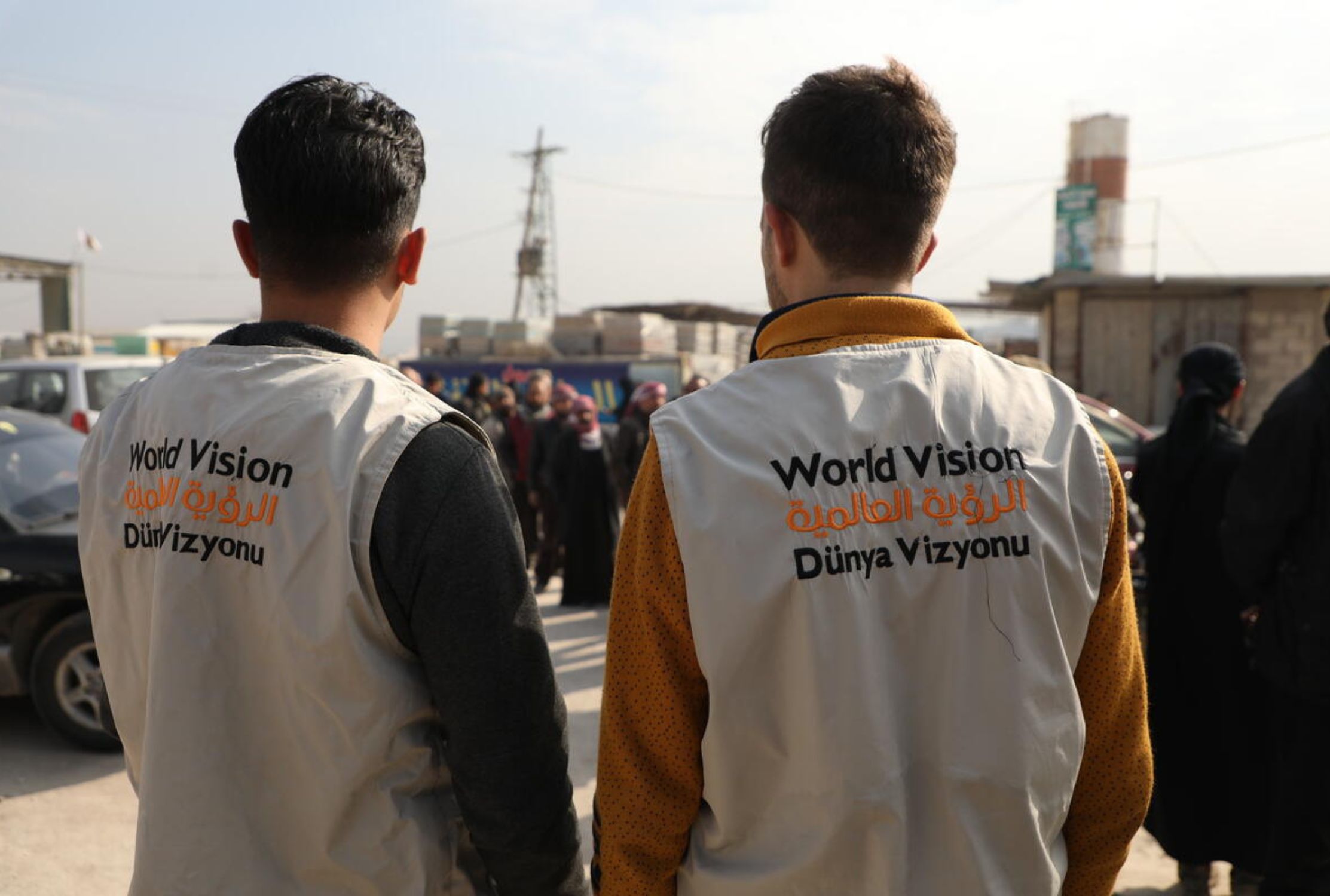 World Vision staff members facing a queue of Syrian people, wearing World Vision branded vests